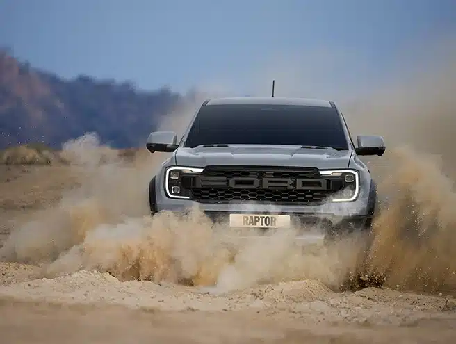Xe bán tải Ford Ranger Raptor màu xám đang vượt địa hình cát bụi mịt mù.