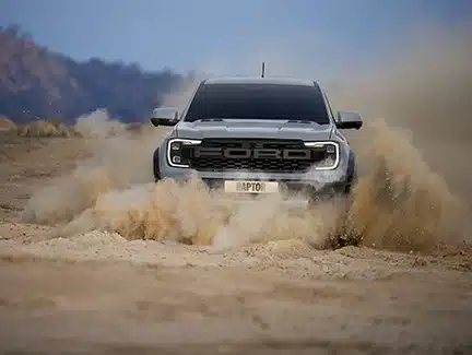 Xe bán tải Ford Ranger Raptor màu xám càn lướt dũng mãnh, bốc bụi mịt mù trên địa hình cát.