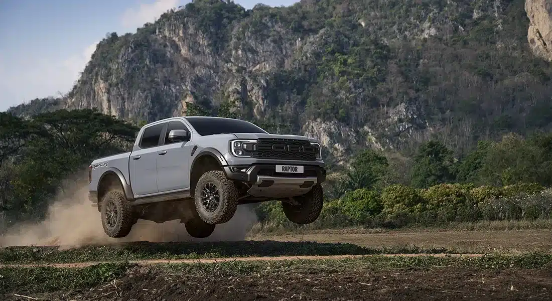 Alt Text: Xe bán tải Ford Ranger Raptor màu xám đang bay trên địa hình off-road đồi núi cát bụi.